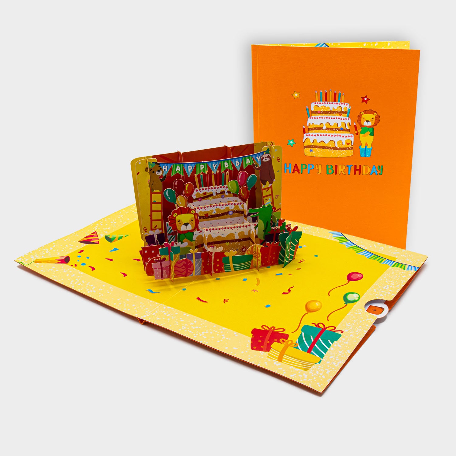 Aufgeklappte 3D Pop-Up Karte mit Geburtstagstorte, Geschenken und Tieren, daneben die zugeklappte Karte mit Torten- und Löwenmotiv auf orangem Cover.