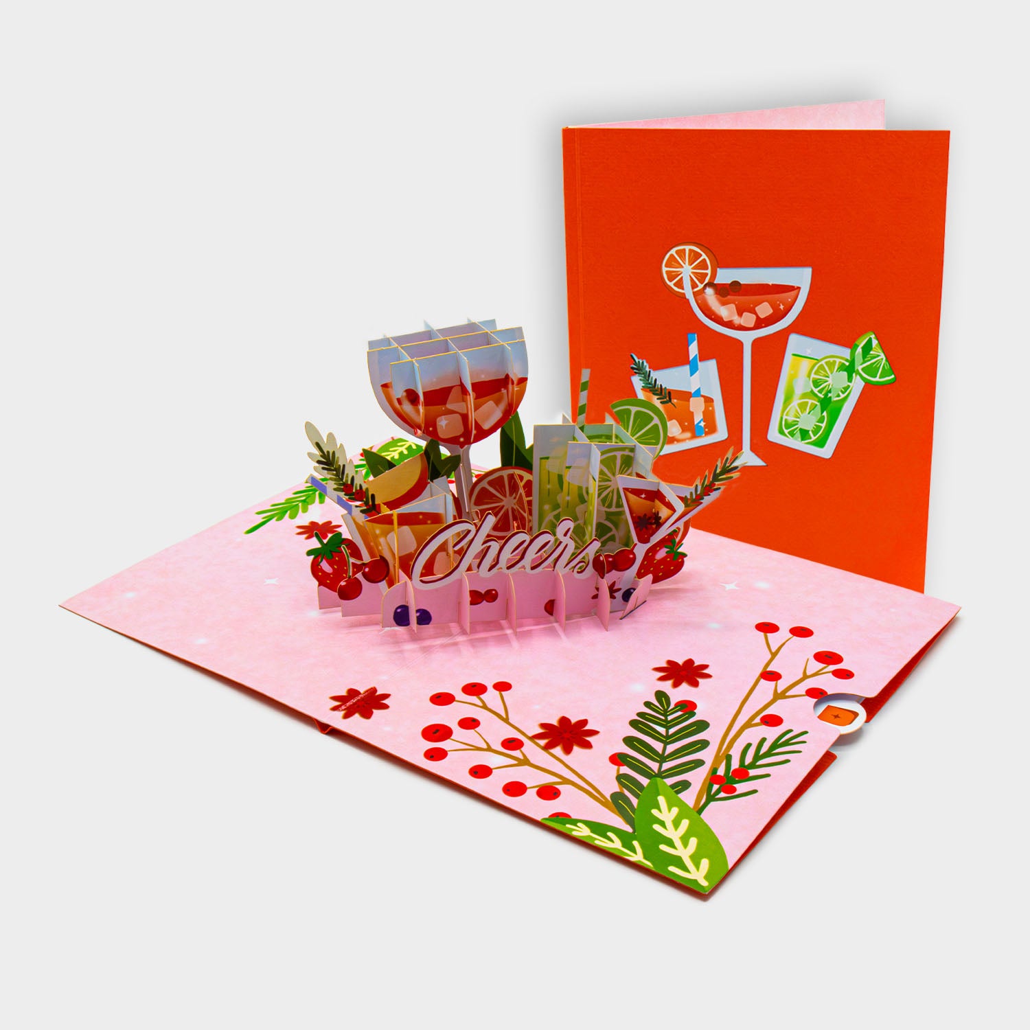 Aufgeklappte 3D Pop-Up Karte mit Cocktailgläsern, Früchten und „Cheers“-Schriftzug, daneben die zugeklappte Karte mit Cocktail-Motiv auf orangefarbenem Cover.