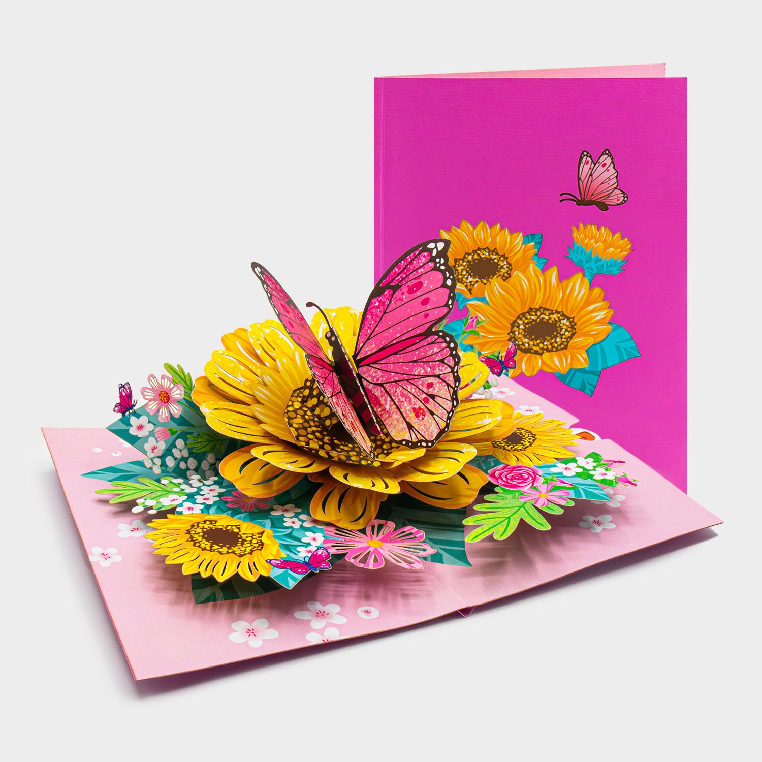 Aufgeklappte 3D Pop-Up Karte mit Sonnenblumen und großem Schmetterling, daneben die zugeklappte Karte mit Blumen- und Schmetterlingsmotiv auf pinkem Cover.
