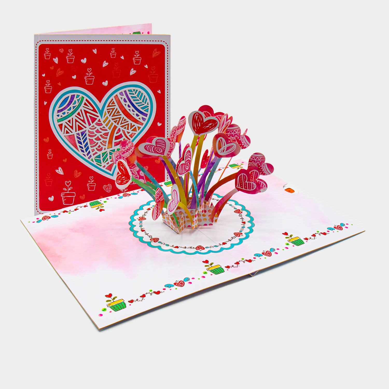 Aufgeklappte 3D Pop-Up Karte mit Herzblumenstrauß, daneben die zugeklappte Karte mit großem Herz-Motiv auf rotem Cover.