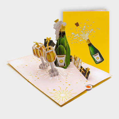 Aufgeklappte 3D Pop-Up Karte mit Champagnerflasche und Gläsern, daneben die zugeklappte Karte mit Sekt-Motiv auf gelbem Cover